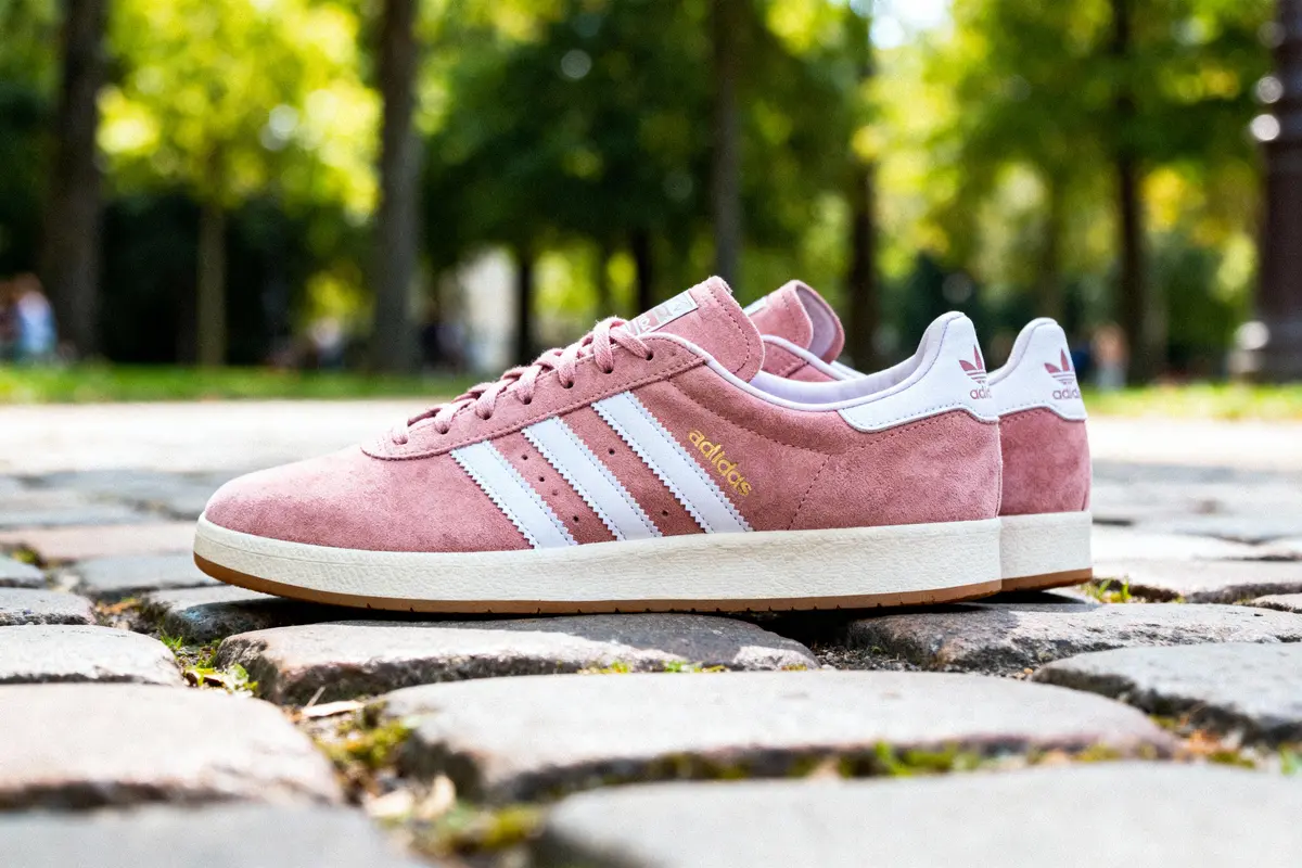Chaussures Adidas roses sur pavés, arrière-plan flou avec arbres verdoyants.
