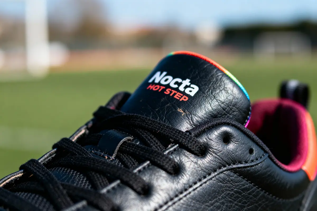 Gros plan sur une chaussure noire Nocta Hot Step, avec fond vert flou.