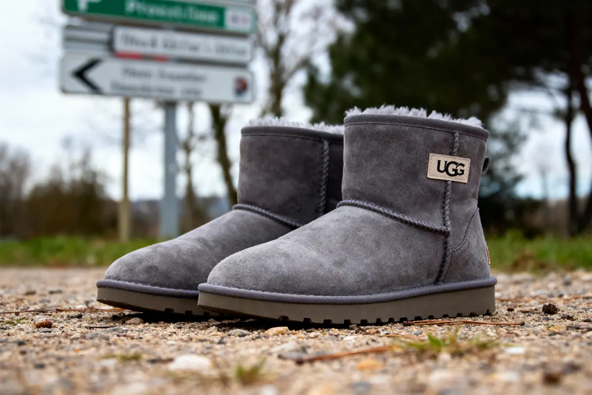 Bottes UGG grises sur sol caillouteux avec panneau de signalisation flou en arrière-plan.