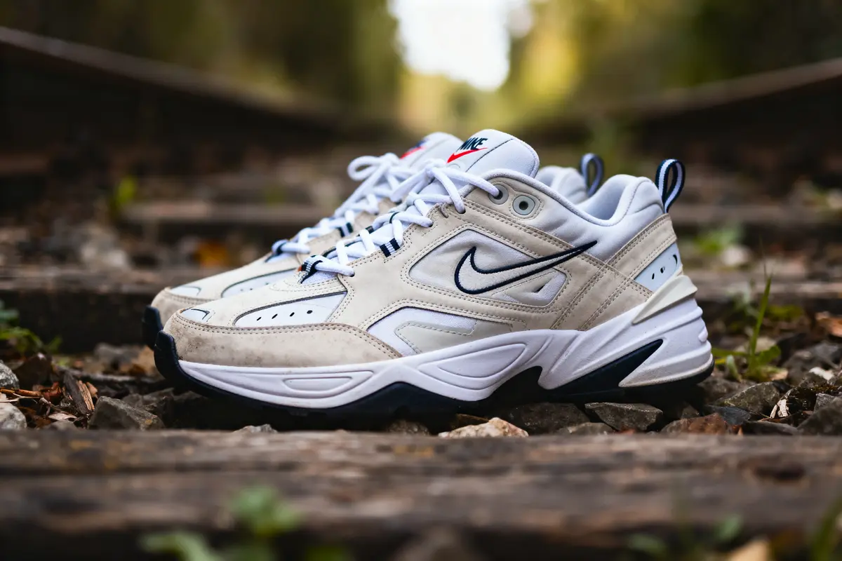 Chaussures de sport blanches Nike sur des rails de chemin de fer en bois, entourées de végétation.