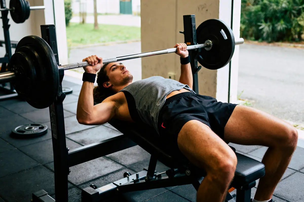 Homme faisant du développé couché avec haltères à la salle de sport, effort musculation, intérieur spacieux.