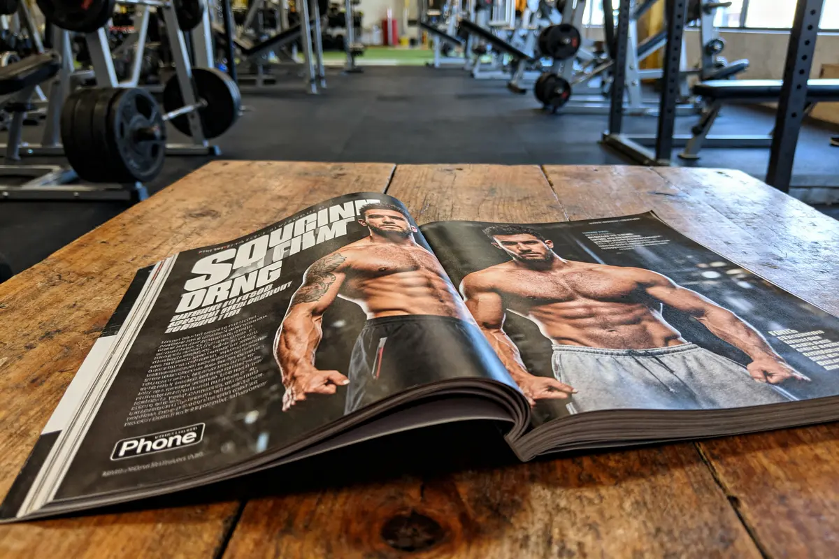 Magazine de fitness sur une table en bois dans une salle de sport, montrant des hommes musclés.