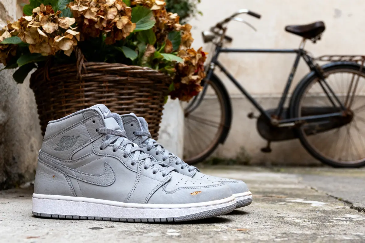 Chaussures grises devant panier de fleurs séchées, vélo ancien en arrière-plan, sur sol en béton.