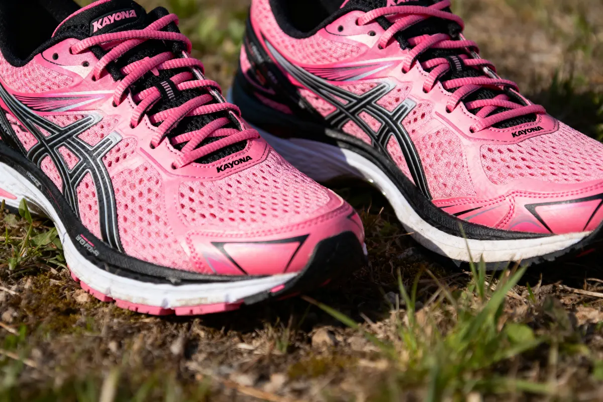 Chaussures de course roses et noires sur l'herbe, en gros plan.