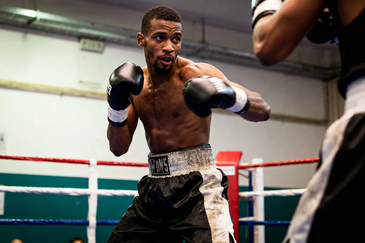 Boxeur en plein combat dans un ring, portant des gants noirs et un short noir et blanc.