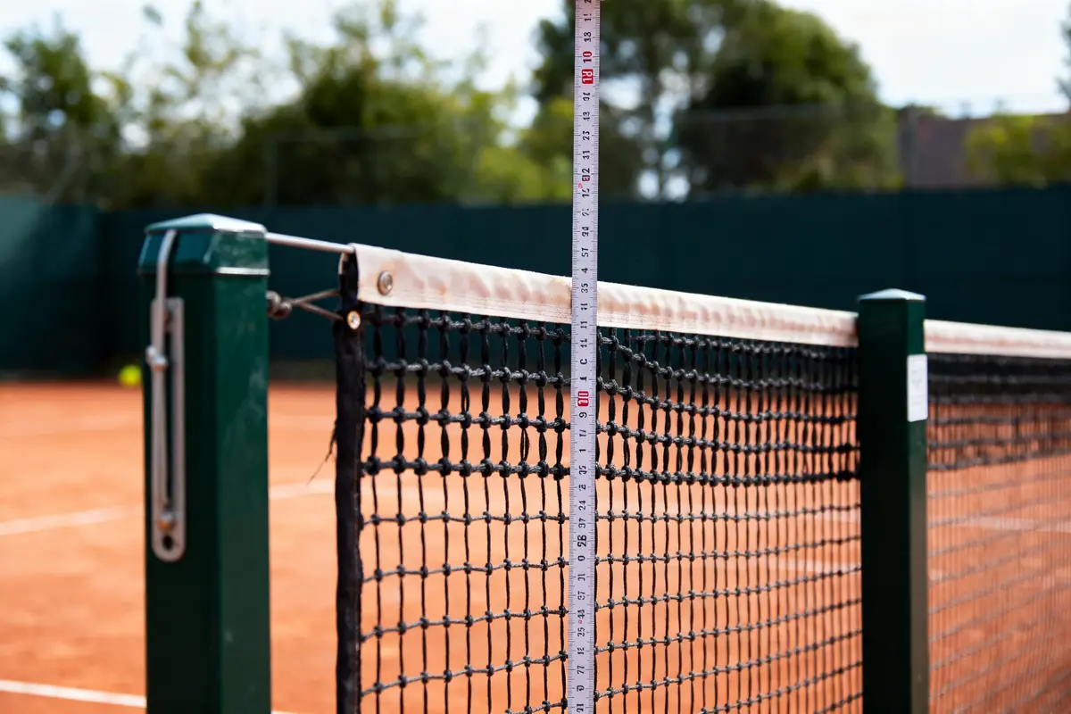 Règle graduée mesurant la hauteur d'un filet sur un court de tennis en terre battue.