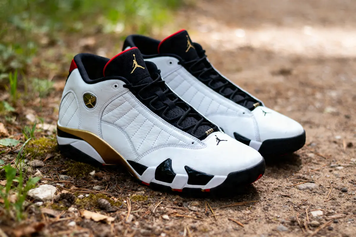 Air Jordan XIV blanches avec détails dorés et noirs sur chemin en forêt