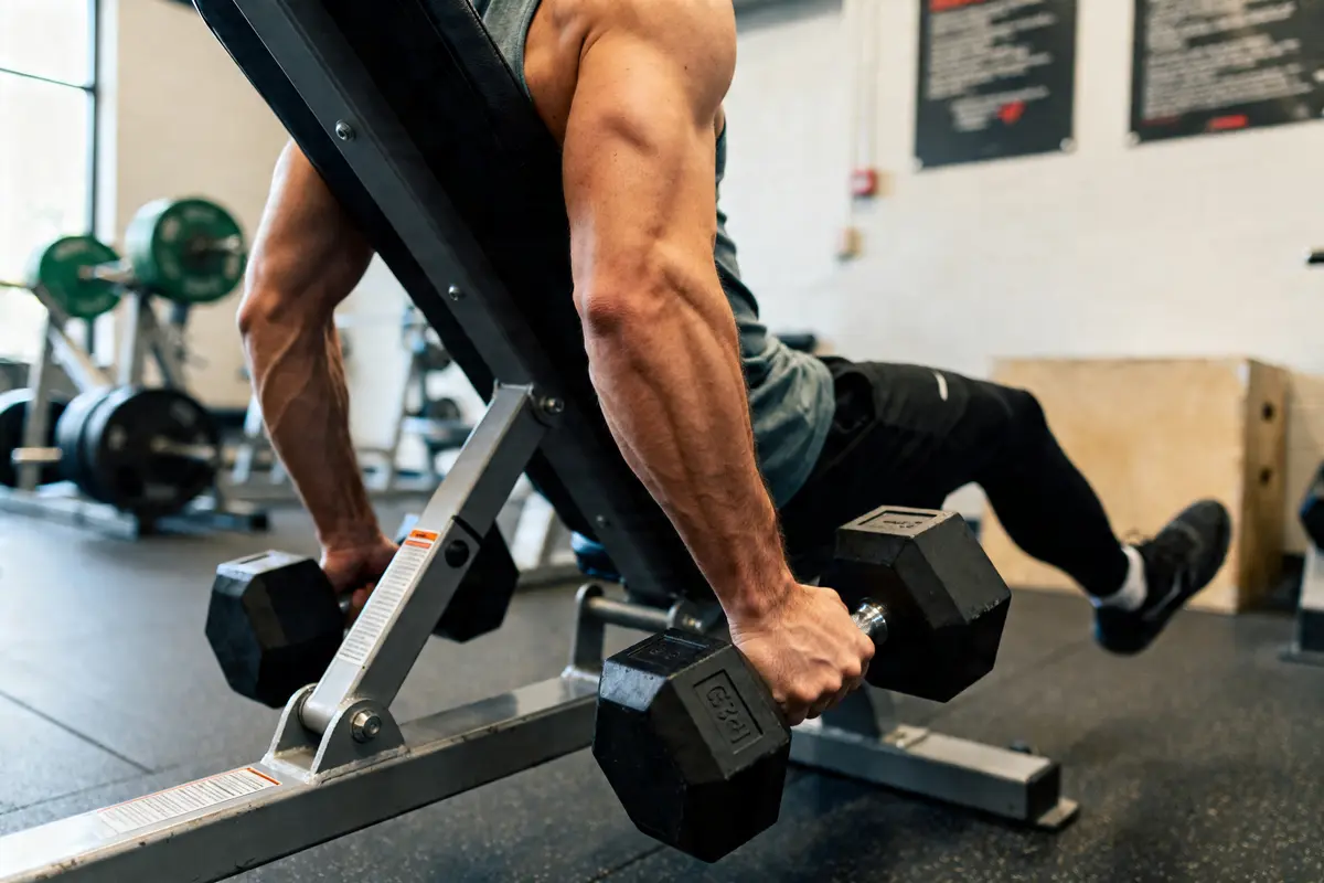 Homme effectuant des spider bicep curls avec haltères sur banc incliné en salle de sport