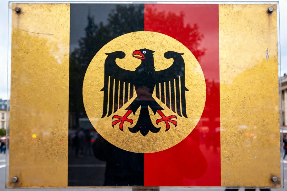 Aigle noir sur fond tricolore, symbole allemand, réfléchissant la scène environnante.
