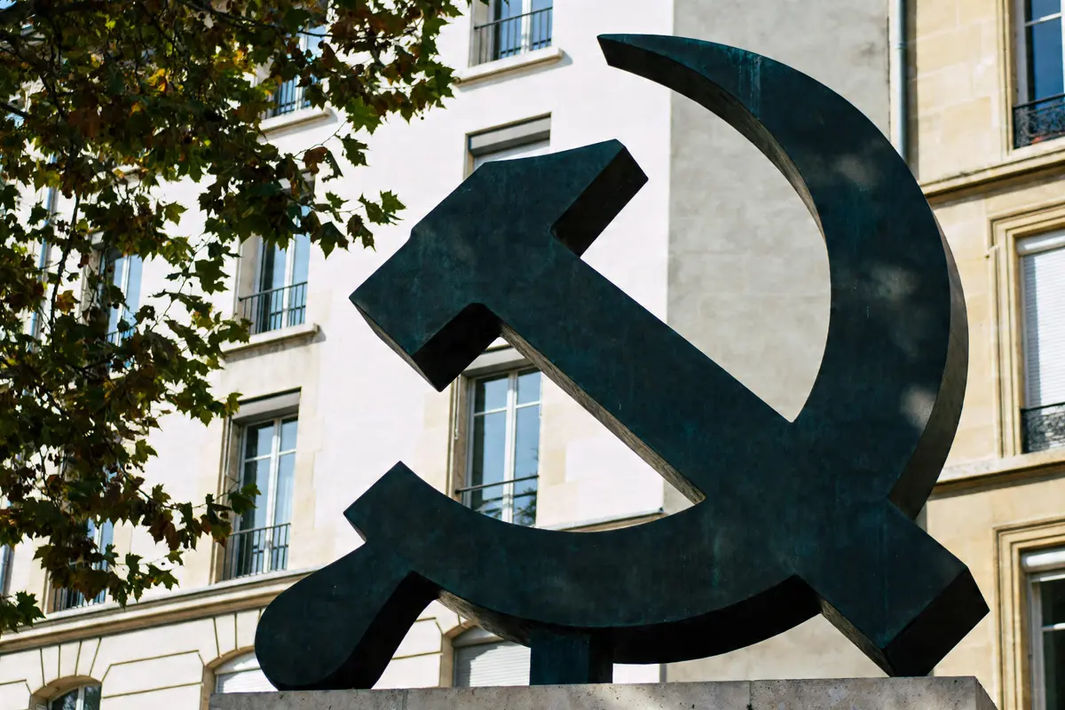 Statue d'une faucille et marteau, symbole du communisme, devant un bâtiment urbain