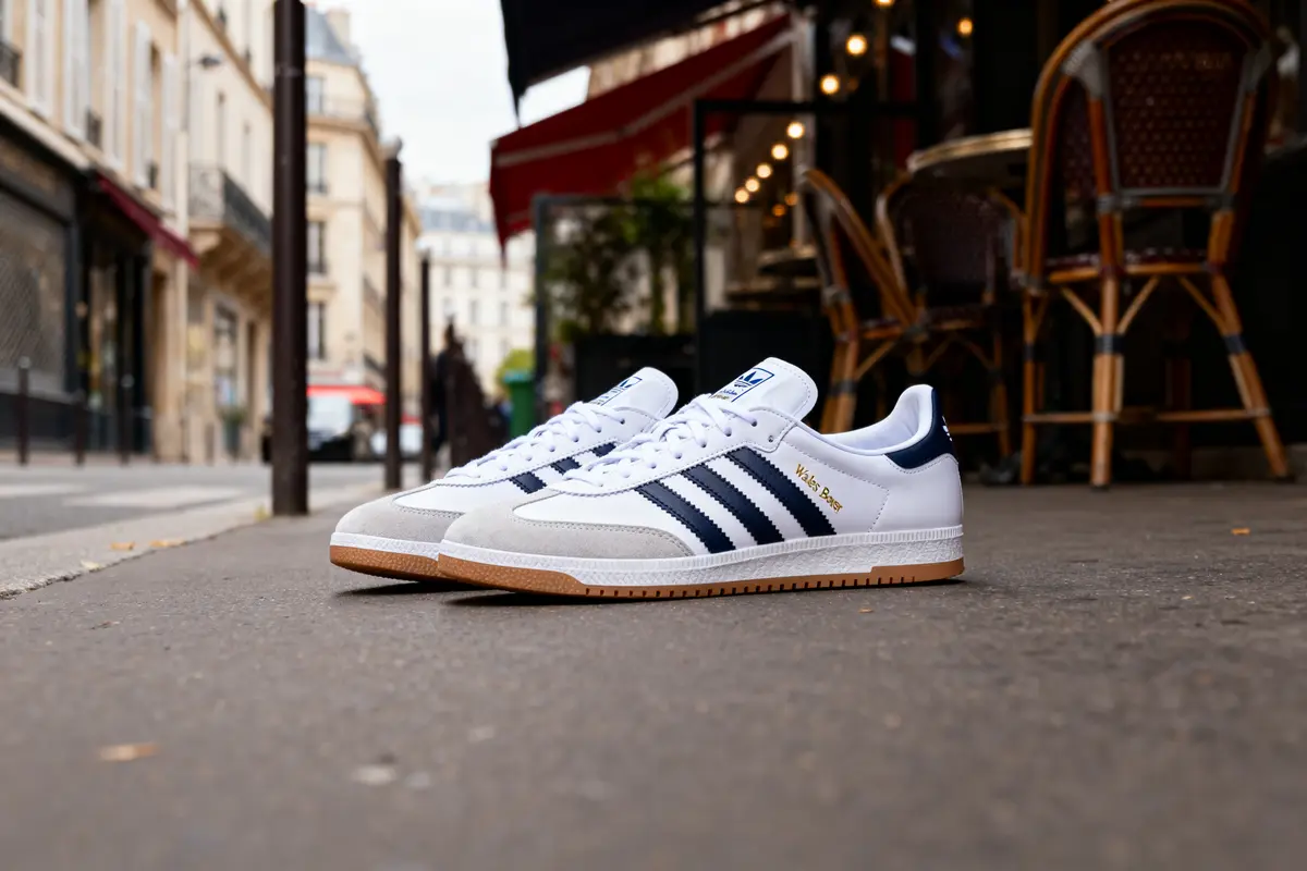 Une paire de baskets blanches avec bandes noires sur rue parisienne, devant terrasse de café.