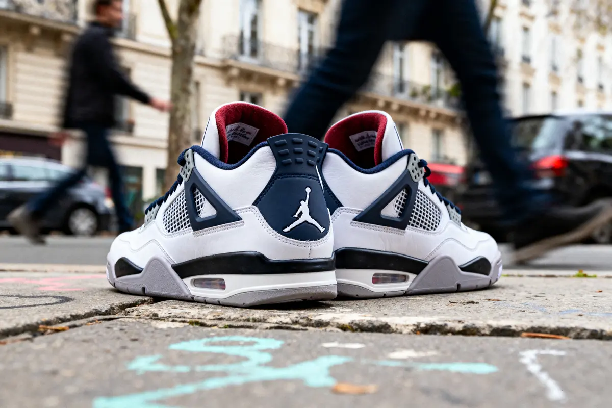 Paire de baskets blanches sur un trottoir, avec des passants flous en arrière-plan dans une rue urbaine.