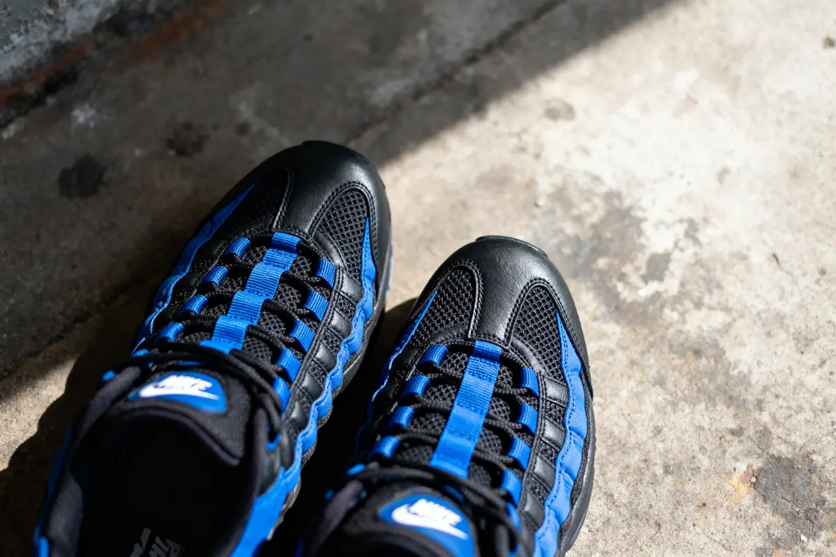 Chaussures de sport noires et bleues posées sur le sol en béton, éclairées par la lumière du soleil.