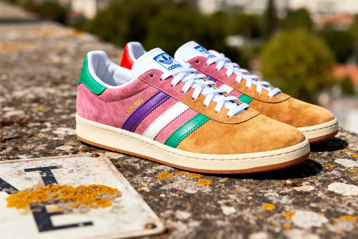 Chaussures Adidas multicolores posées sur un muret ensoleillé, arrière-plan flou de nature.