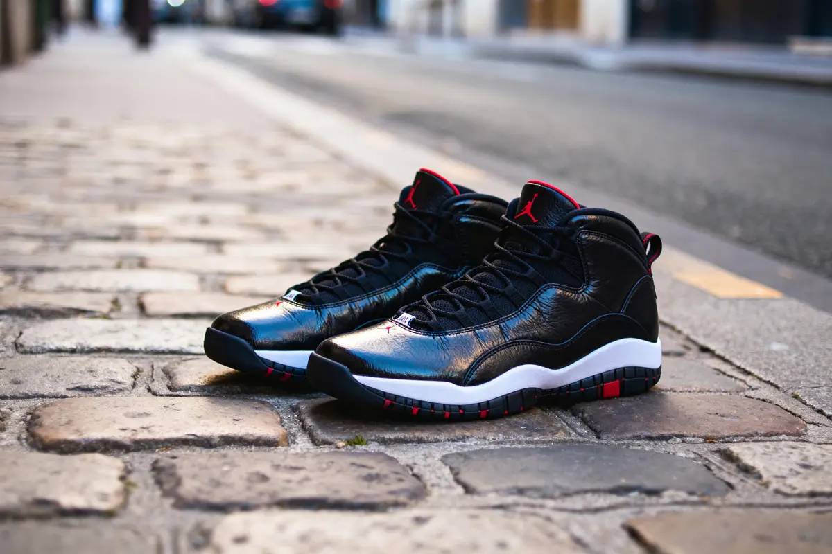 Basketball shoes noires et rouges sur pavés, avec semelle blanche, en extérieur urbain.