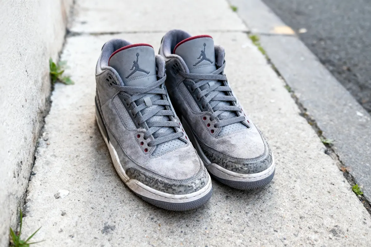 Une paire de baskets grises sur un trottoir en béton. Modèle en daim avec logo visible.