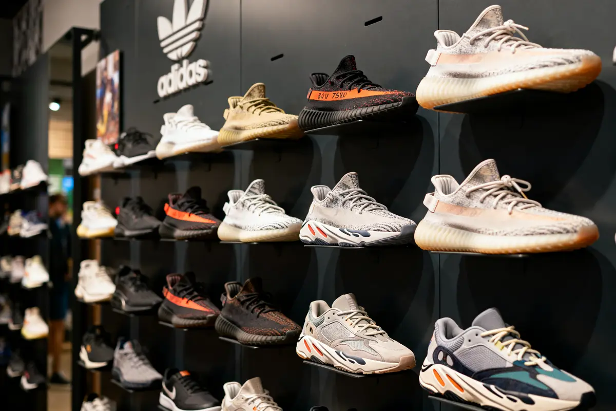 Mur de baskets Adidas exposées, divers modèles et couleurs, logo Adidas visible en arrière-plan.