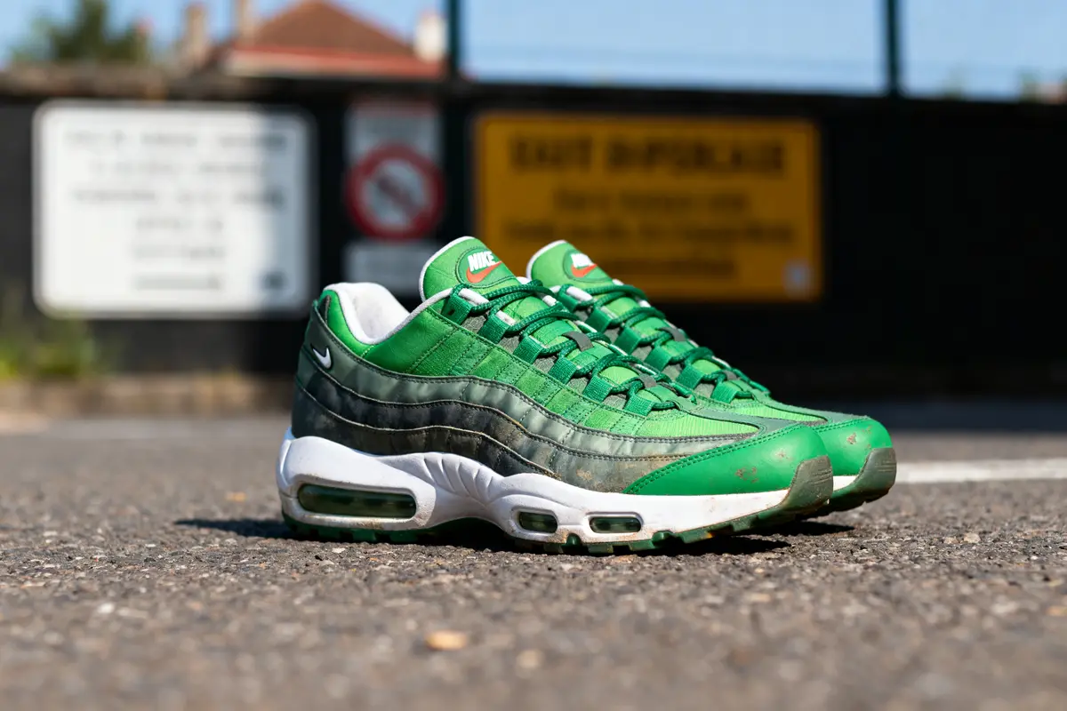 Basket verte Nike Air Max posée sur chaussée, avec panneau flou en arrière-plan.