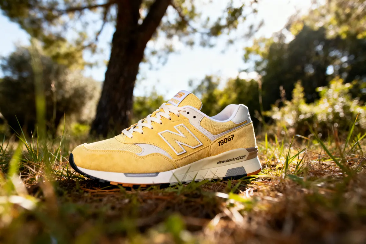 Chaussure jaune New Balance posée dans l'herbe, éclairée par le soleil, avec arrière-plan naturel flou.