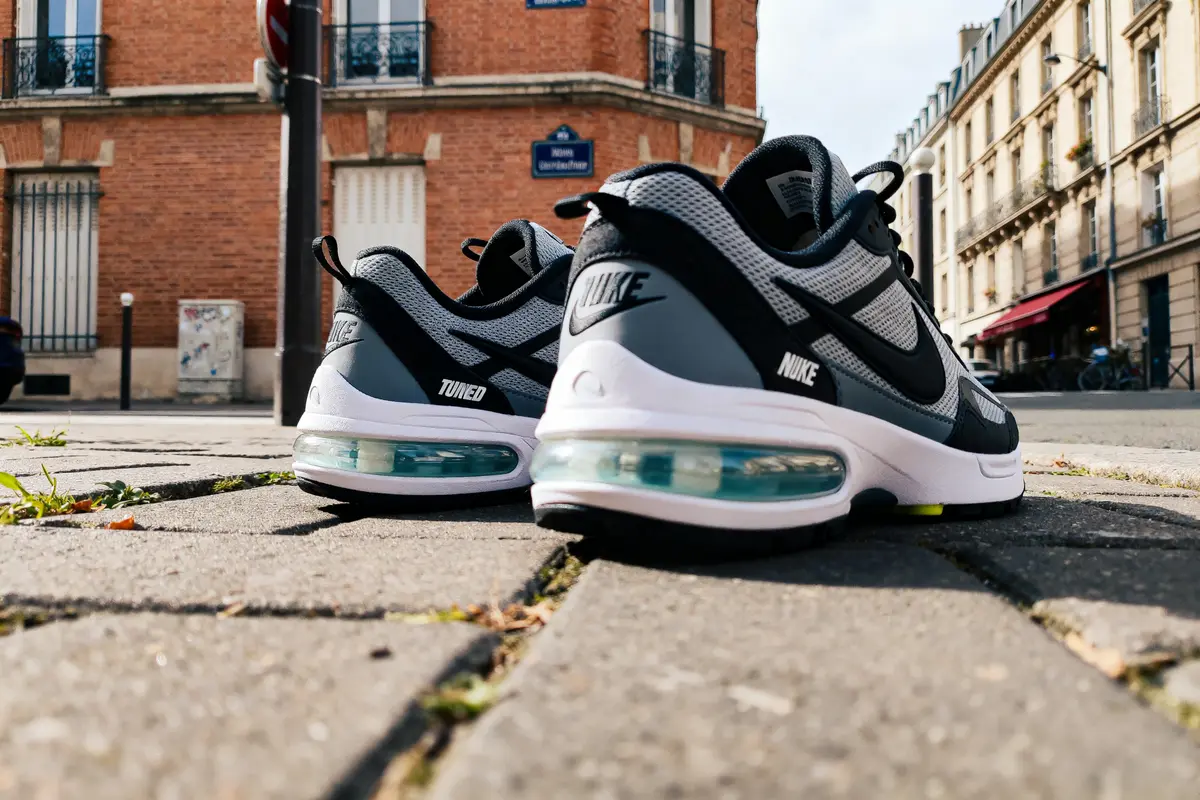 Chaussures de sport noires et grises Nike sur pavés, avec bâtiments en arrière-plan.