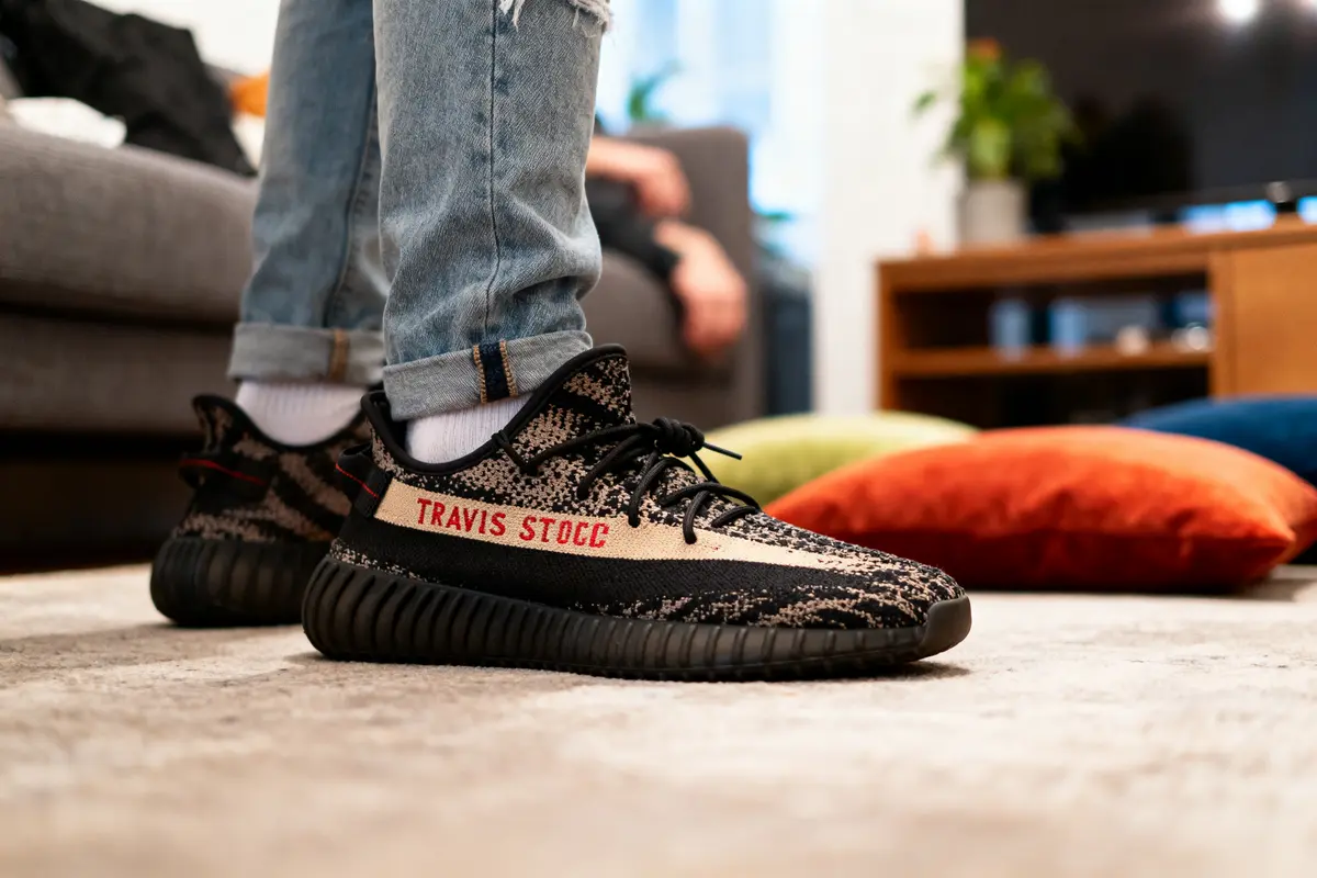 Personne portant des baskets Travis Stocc à motif, jeans déchiré, dans un salon cozy.