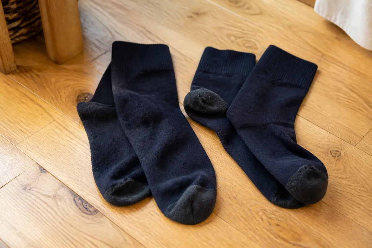 Deux paires de chaussettes noires sur plancher en bois clair, près d'un meuble.