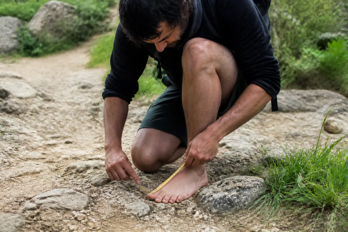 Un homme mesure son pied sur un sentier, pointure en cm indiquée par mètre-ruban