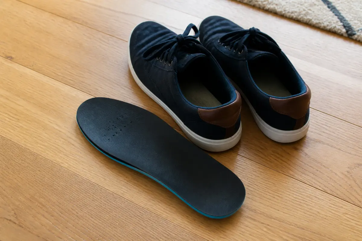 Chaussures bleues et semelle intérieure noire sur plancher en bois clair.