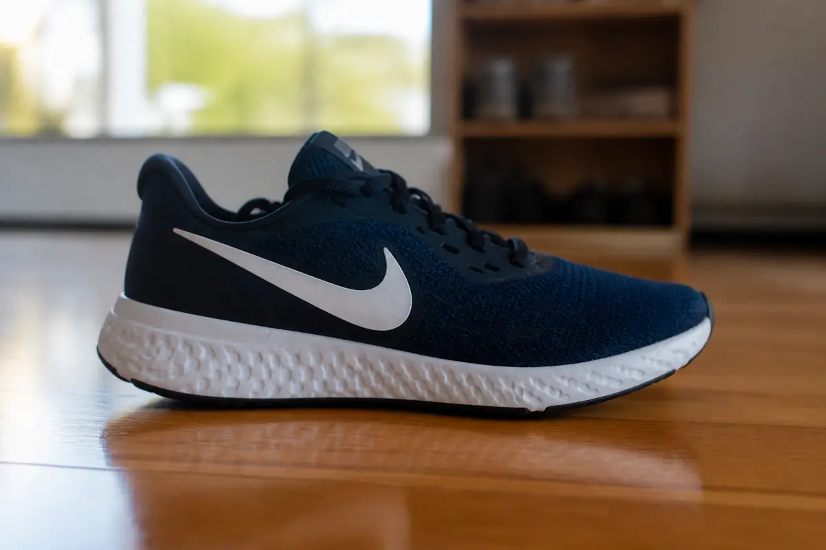 Chaussure de sport bleue avec grande virgule blanche, posée sur un sol en bois.